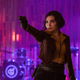 Faye Valentine, in her yellow shirt and purple jacket, aims her gun in front of an empty band stage.